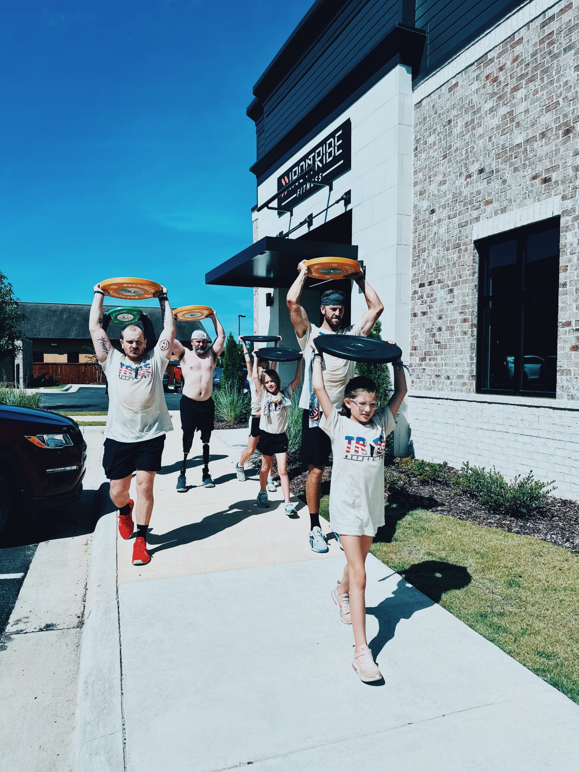 Image of Josh Wetzel with friends and family walking with a weight over their heads for the Wetzel workout outside the Iron Tribe gym.