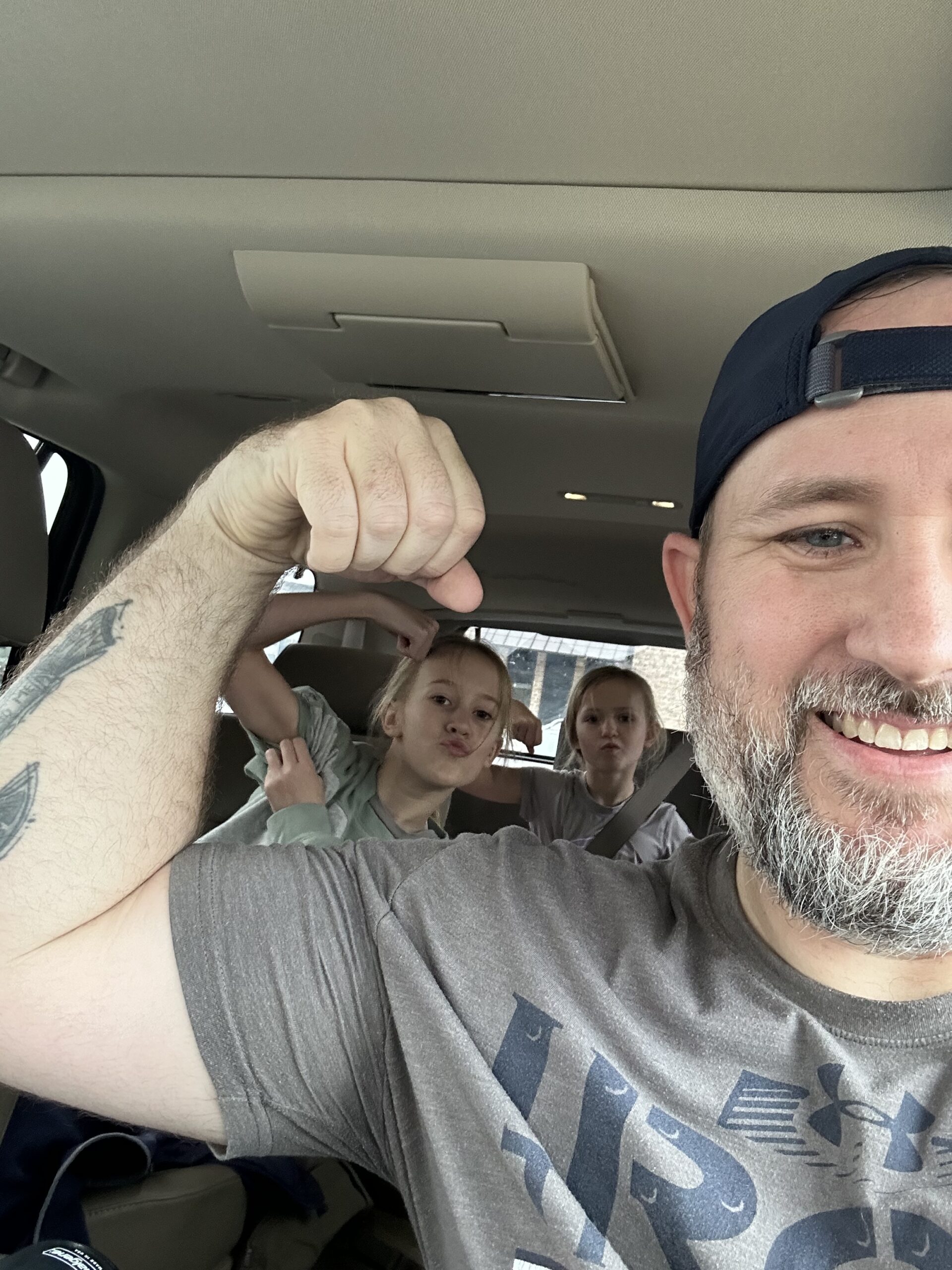 Image of Josh Wetzel and his two children in the car flexing their muscles.